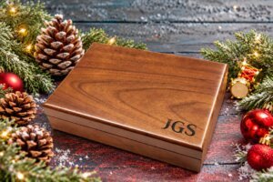 Personalized walnut keepsake box engraved with initials, styled with pinecones, evergreen branches, and Christmas ornaments.