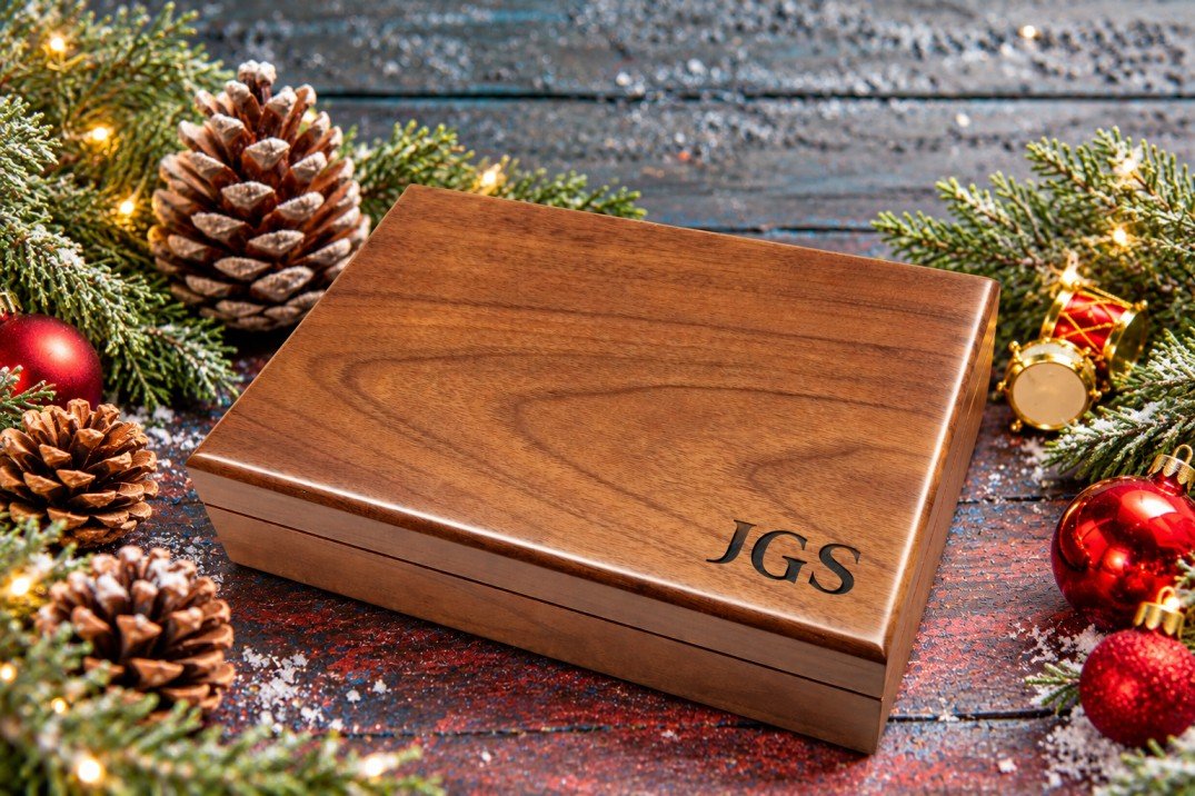 Personalized walnut keepsake box engraved with initials, styled with pinecones, evergreen branches, and Christmas ornaments.